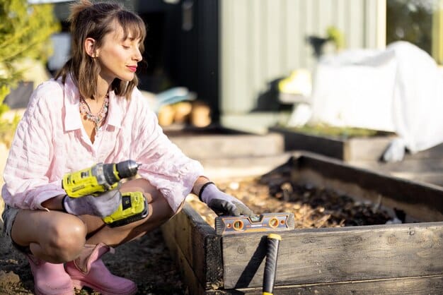 A person constructing a raised garden bed from cedar planks, using screws and a drill. The surrounding area shows gardening tools and other materials organized neatly.