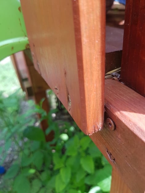 A close-up shot of the corner of a compost bin, showing the wooden frame, hardware cloth for ventilation, and sturdy screw connections.