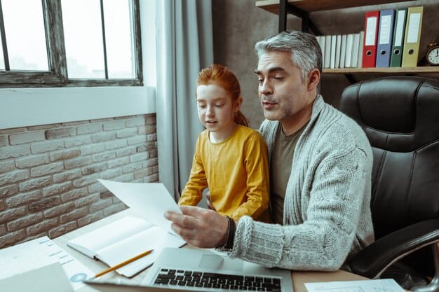 A single dad sitting at his desk, reviewing life insurance quotes on his laptop, with a calculator and financial documents nearby, illustrating the process of comparing insurance options.