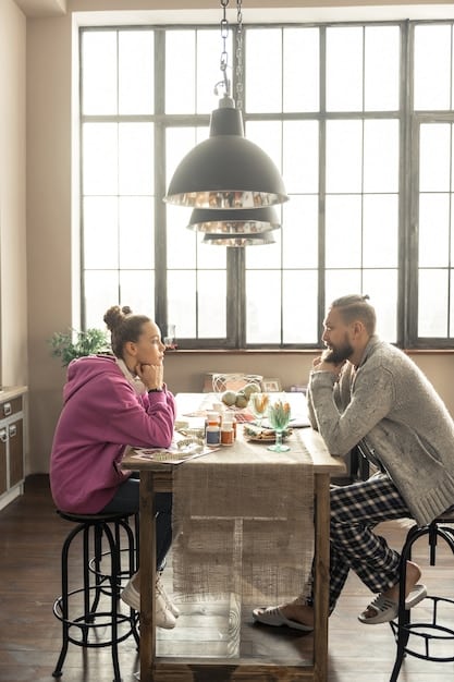 Two parents sitting across from each other at a neutral-toned table in a well-lit room, both holding smartphones, looking at documents, and engaged in a calm discussion. A pencil case and a notebook are also on the table. The image represents respectful communication and planning between co-parents.