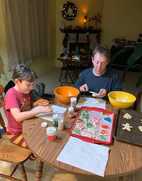 A father and son, both concentrated, are playing a board game at a table. The game board is brightly colored and the pieces are arranged strategically.