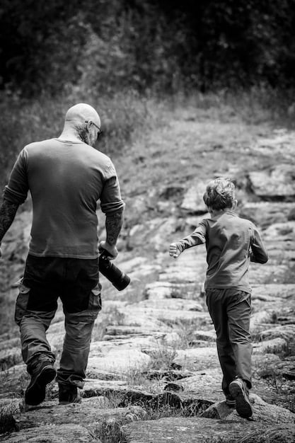 A black and white photo of a boy learning to tie a tie from an older man, perhaps a grandfather or uncle. The focus is on the hands and the patient, guiding nature of the older man.