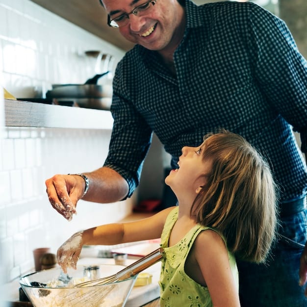 A daughter helps her father with the dishes. Both are smiling.