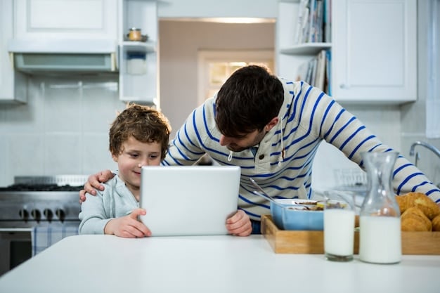 A single dad sitting at a table with his son, both looking at a laptop screen and laughing. The setting is a cozy kitchen with natural light coming in through the window.