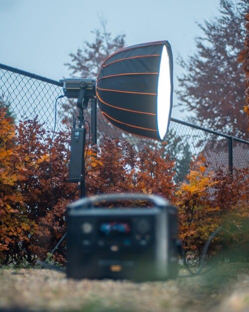 A close-up shot of a compact, affordable outdoor projector casting a bright image onto a white screen in a dimly lit backyard, accompanied by a small Bluetooth speaker, symbolizing a budget-friendly setup.